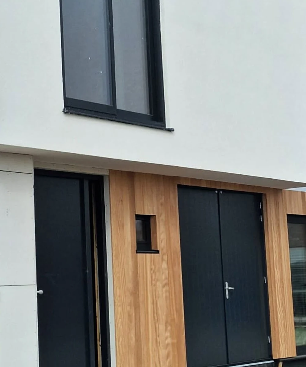 Facade detail showing entrance zone, black joinery and vertical timber cladding