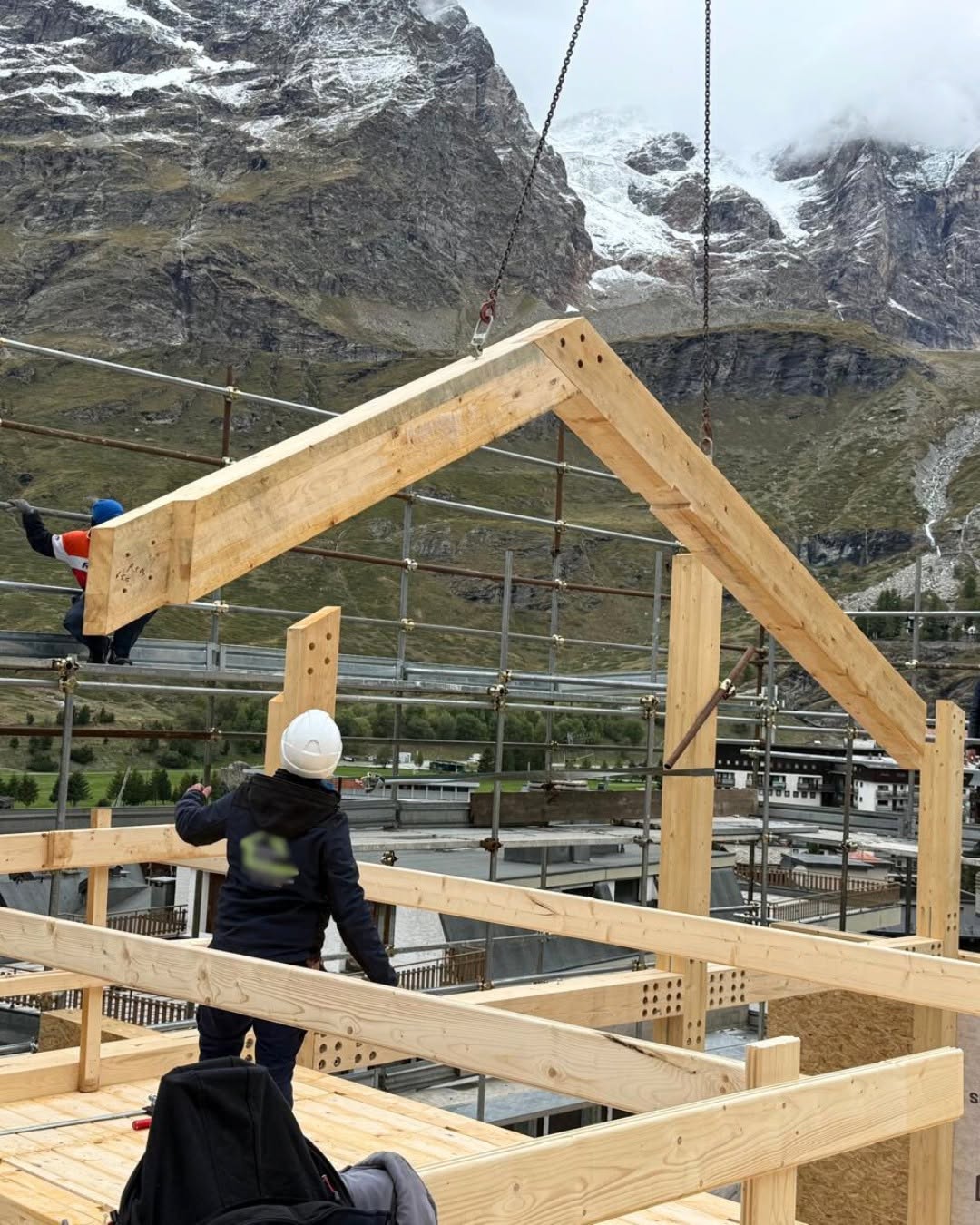 Timber roof structure being lifted into position on a mountain construction site